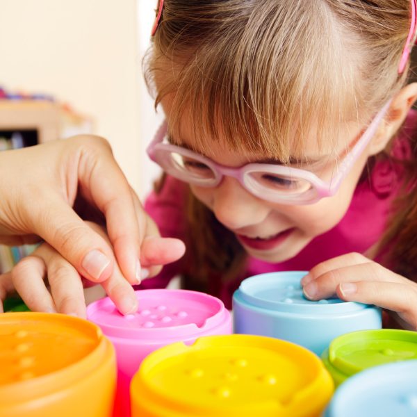 Smiling child with disability touching textured cups with her teacher
