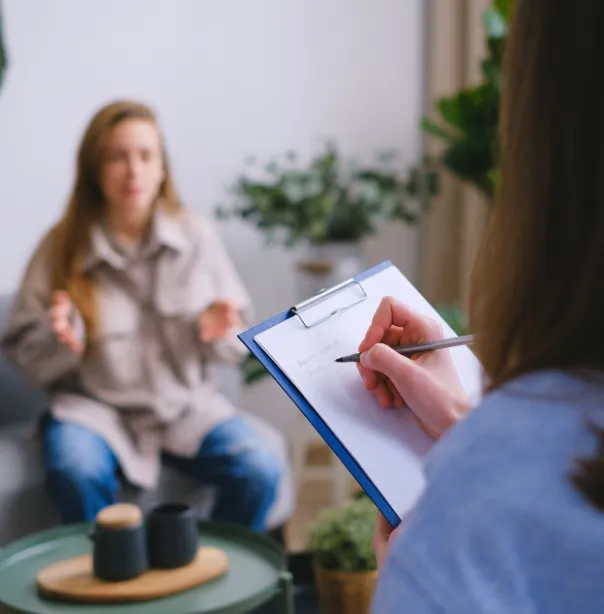 Person talking to a therapist who is taking notes on a clipboard during a counseling session.