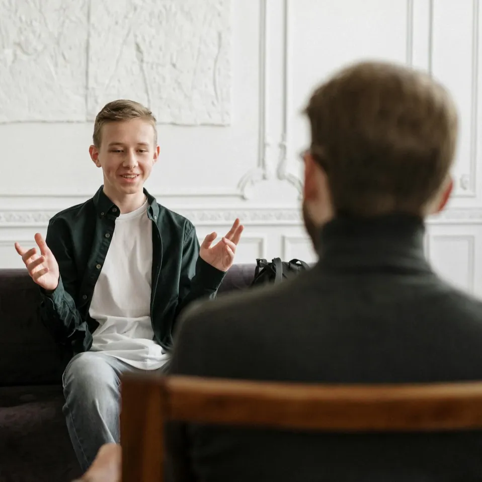 A young person talks and gestures while sitting across from another adult in a conversation.