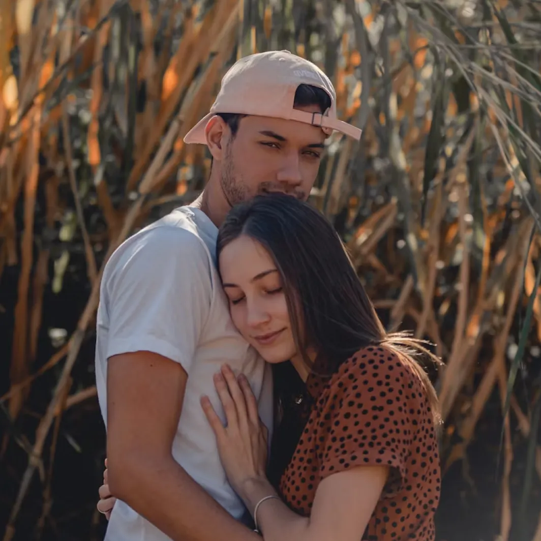 A couple embraces outdoors; the woman leans on the man's chest with her eyes closed.