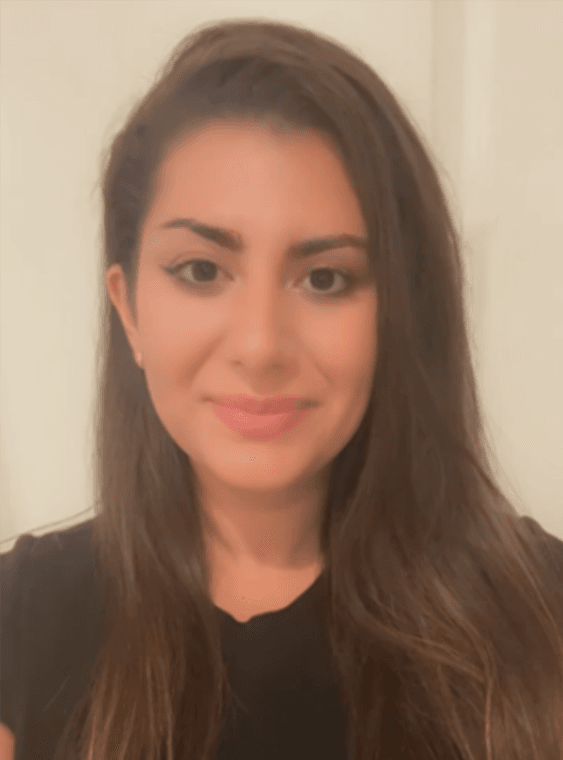 tamara A woman with long brown hair and a black top smiles at the camera against a light background.