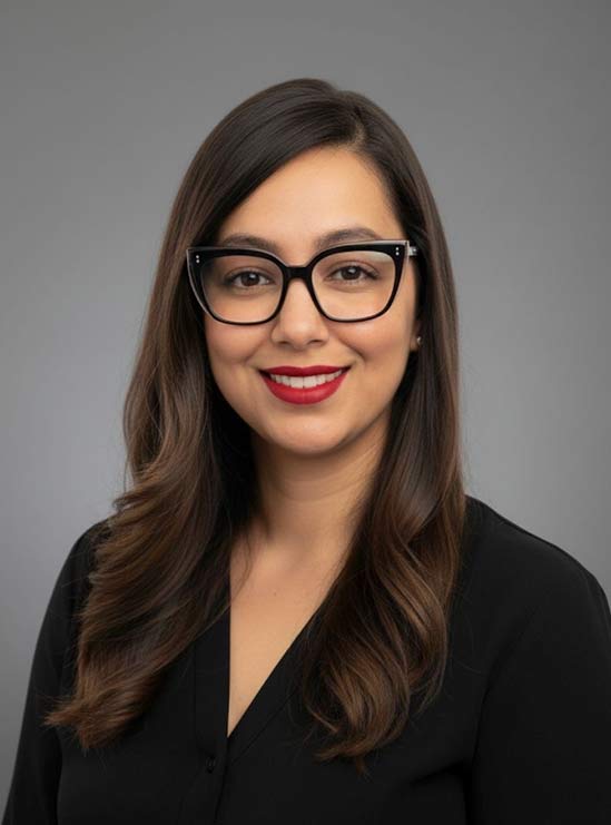 veronica Woman with long brown hair, black glasses, red lipstick, and black blouse smiling in front of a gray background.