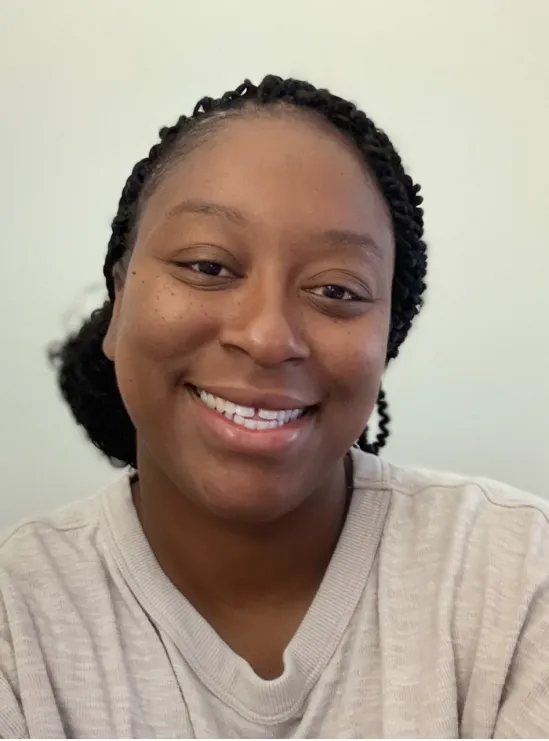 Shantel Castle A woman with braided hair smiles at the camera, wearing a light-colored sweater against a plain background.